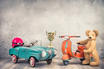 Poster Retro antique aquamarine rusty pedal car from 60s, red helmet with goggles, race winner golden cup, old orange children's scooter and Teddy Bear plush toy front loft wall. Vintage style filtered photo © BrAt82