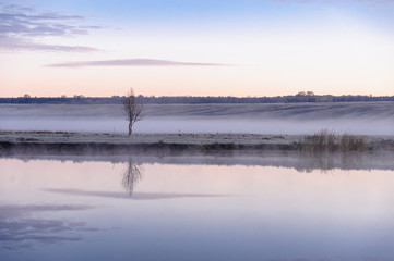 Dawn over the river on a summer morning, fog over the field, grass with hoarfrost