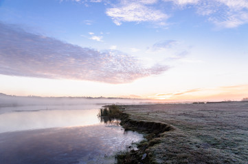 Dawn over the river on a summer morning, fog over the field, grass with hoarfrost