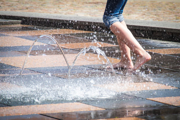 Girl walks barefoot on a fountain in summer heat