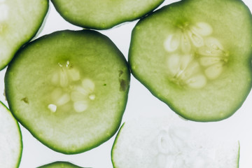 green translucent slices of cucumber on the background of bright white light close-up. transparent discs of vegetables. texture of kaleidoscope patterns in macro