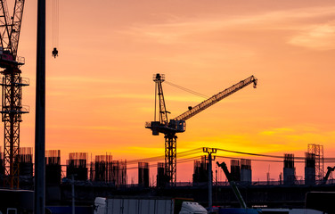 Construction site with crane and sunset sky. Real estate industry. Crane use reel lift up equipment in construction site. Building made of steel and concrete. Crane work against orange sunset sky.
