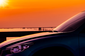 Side view of SUV car with sport and modern design parked on concrete road by the sea at sunset. Hybrid and electric car technology. Travel on vacation at the beach. Road trip. Automotive industry.