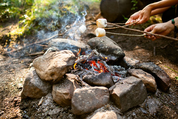 A girl sits by the fire in the woods drinking tea and roasting marshmallows