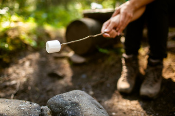 A girl sits by the fire in the woods drinking tea and roasting marshmallows