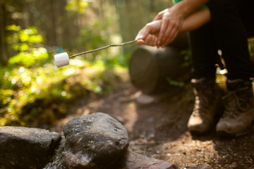 A girl sits by the fire in the woods drinking tea and roasting marshmallows