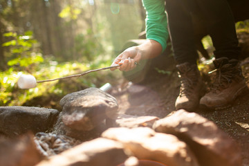 A girl sits by the fire in the woods drinking tea and roasting marshmallows