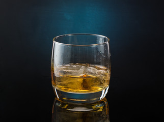 A glass of whiskey with ice on a dark color photo with splashes from falling ice