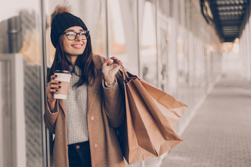 Beautiful fashionable woman drink coffee walking near mall with shopping bags.