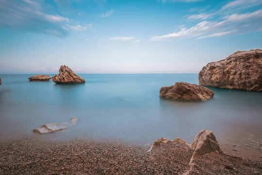 Long exposure image of blue sky and sea with rocks in sunset scenery background. Sunset pebble sea beach among rocks and stones. Antalya. Turkey.