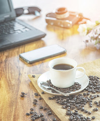 coffee cup whit coffee bean on Wood photographer desk table with film camera, laptop computer.