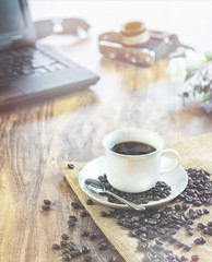 coffee cup whit coffee bean on Wood photographer desk table with film camera, laptop computer.