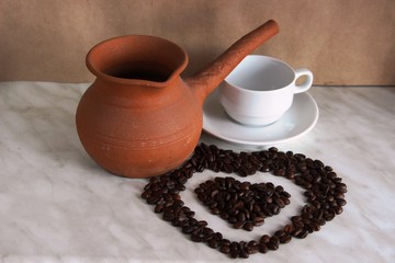 brown clay Turk for cooking coffee, white Cup and saucer and roasted coffee beans in the shape of a heart, selective focus