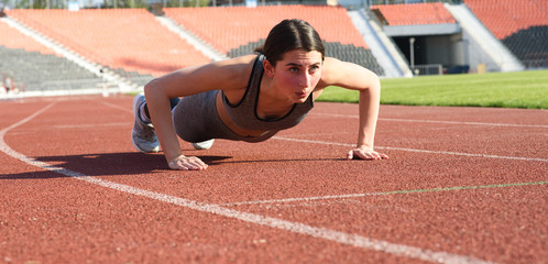 Obraz premium Beautiful and athletic girl push ups at the stadium
