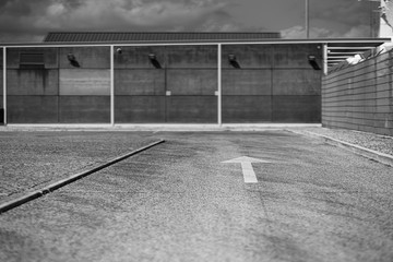 Black and white view of an asphalt road with selective focus on a white arrow road marking on it...
