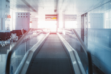 Fototapeta premium View of a modern travelator stretching into the vanishing point indoors of a railways station depot; moving walkway inside of a departure area of an airport terminal with a reddish flare at the end