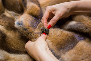 Tailor sewing button of fur coat