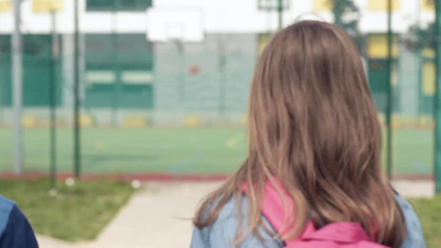 Back view - two schoolchildren go to school with backpacks. Cute children - teen girl and boy with bags Back to school. Concepts of friends, childhood and education.