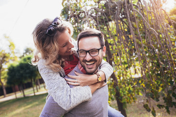 Couple having fun outdoor. Man giving piggyback to woman in park.