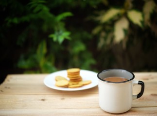 a cup of hot coffee on wooden table in green garden.