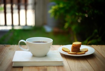 a cup of hot coffee on wooden table in green garden.