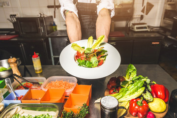 Professional chef cooking in the kitchen restaurant at the hotel, preparing dinner. A cook in an apron makes a salad of vegetables and pizza.