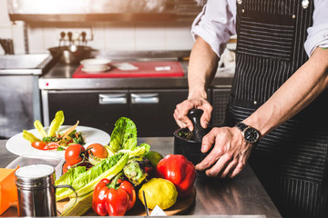 Professional chef cooking in the kitchen restaurant at the hotel, preparing dinner. A cook in an apron makes a salad of vegetables and pizza.