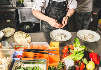 Professional chef cooking in the kitchen restaurant at the hotel, preparing dinner. A cook in an apron makes a salad of vegetables and pizza.