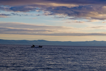 a fisherman in his boat on the sea. in the back an isle in the late afternoon about sunset