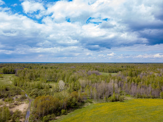 Aerial view of a landscape with green fields and forest under gray clouds and clouds on a warm spring day. Nature and the environment without people and harmful emissions.