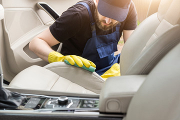 Cleaning service. Man in uniform and yellow gloves washes a car interior in a car wash. Worker...