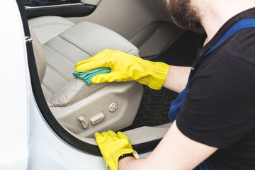 Cleaning service. Man in uniform and yellow gloves washes a car interior in a car wash. Worker washes the chairs of the leather salon