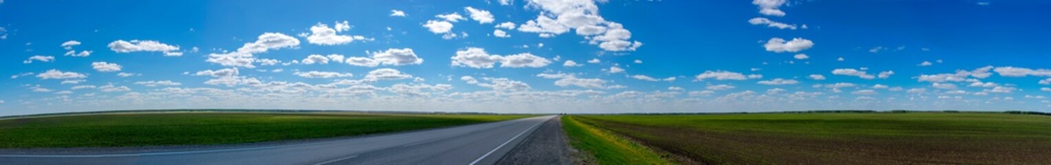 Panorama of the road under a cloudy sky. Blue sky and green fields. Panorama Highway.