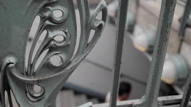 Unrecognized people descend into the Paris metro. In the foreground forged railings. Close-up. Slow Motion.