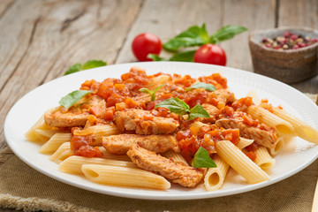 Penne pasta, chicken or turkey fillet, tomato sauce with basil leaves on old rustic wooden background. Close up, side view