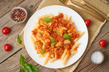 Penne pasta, chicken or turkey fillet, tomato sauce with basil leaves on old rustic wooden background. Top view