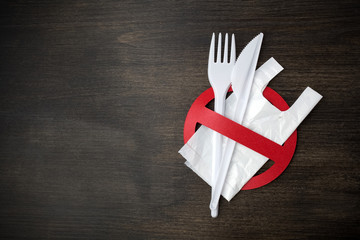 White plastic tableware on a wooden background as a symbol of environmental pollution. Ban single...