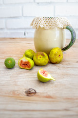 Over ripe and halved figs together with an antique enamel jug and lace doily on a raw wood surface