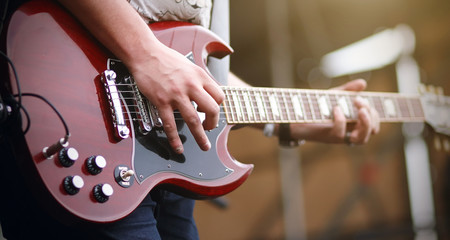 A man plays a melody on a red gothic six-string electric guitar on stage at a concert