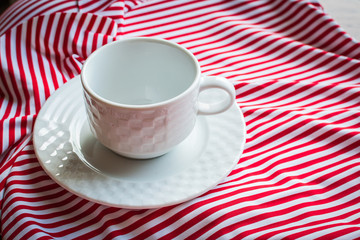 Empty mug for tea and saucer on striped swimsuit.