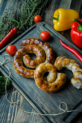 Fried sausage with herbs and spices, wooden background. Ring of baked homemade sausage. Served on a wooden board with greens and vegetables. Side view.