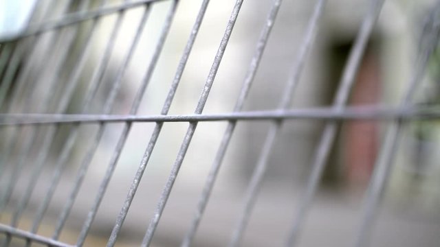 Blurred background. The fence enclosing. Bokeh walking. People are moving. Blurry footage. Metal fence. Although people on the street near the fence. No focus. A group of people walking at the fence. 
