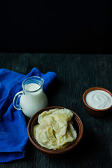 Dumplings with potatoes and cabbage. Sour cream, milk and greens. Traditional dish of Ukraine. Dark wooden background.