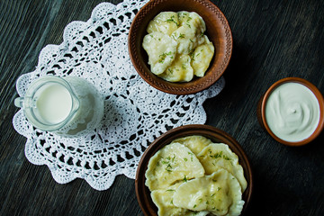 Dumplings with potatoes and cabbage. Sour cream, milk and greens. Traditional dish of Ukraine. Dark wooden background.