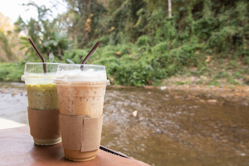 Iced coffee and iced green tea on desk, beautiful nature background