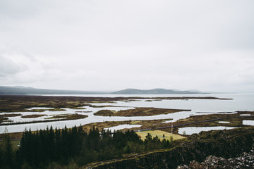 Cold bleak landscapes of Thingvellir National Park in Iceland in spring. Beautiful nature with pale green grass, rivers, and snowy peaks of high mountains.