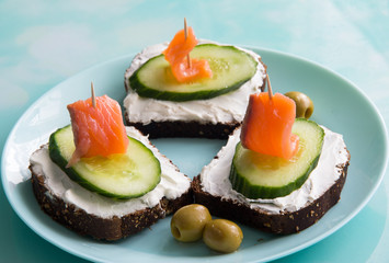 Sandwich with red fish, cucumber, cottage cheese and olives on a plate