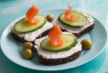Sandwich with red fish, cucumber, cottage cheese and olives on a plate