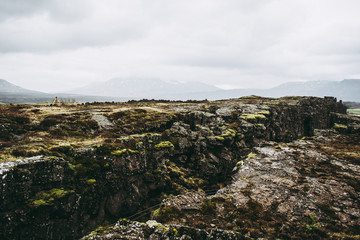 Fototapeta na wymiar Cold bleak landscapes of Thingvellir National Park in Iceland in spring. Ancient rocks against dark misty mountains and gray sky