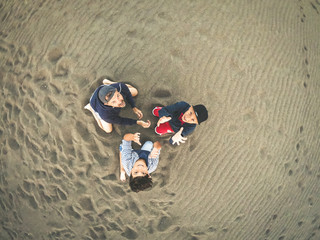 Father and sons playing on the beach taking selfie with action cam Unusual point of view of two young boys and a man on the beach looking up on the camera View from top of a group of people having fun